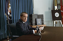 Nixon l'air grave est assis à son bureau devant une pile de classeurs.