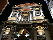 Vue en contre-plongée de nuit d'une façade savamment éclairée de type baroque possédant fronton, décorations et statues.