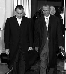 Photographie de deux hommes portant de longues manteaux quittant un bâtiment