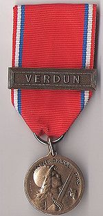 Médaille métallique ronde suspendue à un ruban rouge.