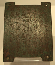 Photographie d'une petite plaque de bronze gravée de sinogrammes anciens.