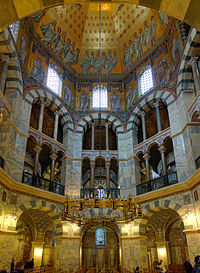 Photographie de l'intérieur d'une chapelle de style carolingien avec un large lustre doré suspendu au-dessus d'un autel.