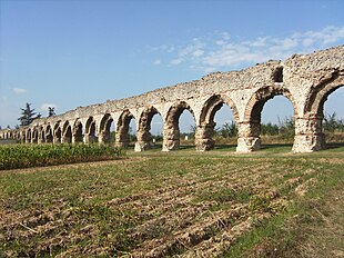 Photographie d'un aqueduc porté sur des arches de briques traversant un champ.