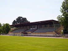 Vue d'un petit stade de rugby. Une tribune couverte en béton en arrière-plan