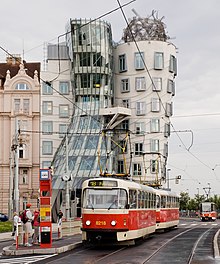 Un vieux tramway rouge et crème au premier plan devant un bâtiment très moderne de verre et de béton.