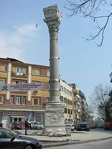 Photographie d'une colonne en pierre située au milieu d'un carrefour urbain.
