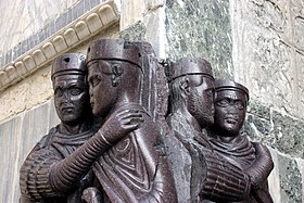 Sculpture située au coin d'un bâtiment aux murs en marbre représentant quatre hommes portant des toges et des épées. Les statues sont quasiment identiques et regroupées par deux.