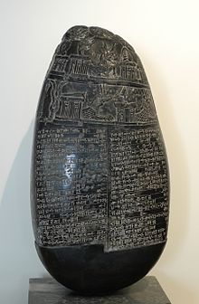Photo du « caillou Michaux », pierre noire aplatie, gravée de deux colonnes en cunéiforme surmontées d'illustrations