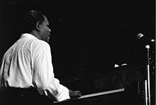 Photo noir et blanc d'un homme noir américain assis au piano, en chemise blanche