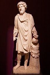 Statue en marbre de Marc Aurèle en toge et debout. Sa main gauche est posée sur une armure.