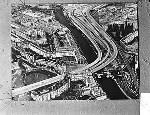 Montage photographique en noir et blanc d'une ville, composée de bâtiments datés majoritairement du début du vingtième siècle, et traversée par une autoroute.