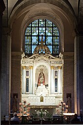 Photographie de la chapelle de Notre-Dame des Miracles et des Vertus. La statue de la Vierge à l’Enfant, l'un et l’autre couronnés, drapée dans un manteau rouge, est placée au centre d'un retable en marbre blanc. Un vitrail emplit la baie au-dessus du retable. Des fleurs et de nombreux cierges se trouvent devant l’autel. Les murs de la chapelle sont couverts d’ex-voto. Deux fidèles prient devant l’autel.