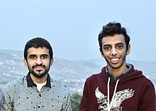 Two young men, one in a collared shirt and one in a maroon hoodie, facing the camera