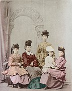 Photo de cinq filles japonaises en costumes de la Belle Époque. Quatre sont assises et une, debout au centre.