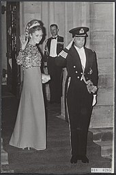Image montrant un couple debout composé d'une jeune femme qui salue de la main droite et d'un homme en tenue d'officier de marine faisant le salut militaire.