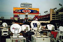 Camions avec des antennes colorées à l'extérieur du stade Raymond James Stadium indiquée par une grande pancarte.