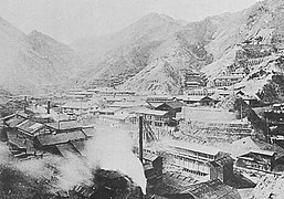 Photo d'un paysage de montagne. Les flancs sont remplis de bâtiments industriels, une fumée monte au premier plan.