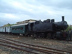 Locomotive à vapeur noire dans la gare de Massaoua tirant deux wagon vert et blanc.
