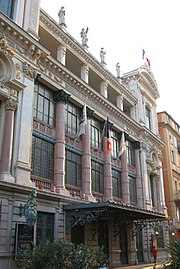 Vue d'un bâtiment de style italien du XVIIIe siècle à colonnes et grandes baies vitrées et statues sur son toit plat.