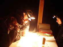 Plusieurs personnes penchées sur une table regardent des papiers à la lueur de lampes frontales.