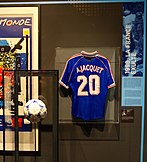 Ballon de la finale de la Coupe du monde de football 1998, et maillot Bleu floqué au nom d'Aimé Jacquet avec le numéro 20.