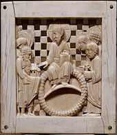 Plaque en ivoire gravée représentant un homme barbu en toge assis sur une sorte d'anneau. Plusieurs personnages également en toge l'entoure et l'un d'eux tient la maquette d'une église.