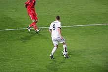 Photo de Karim Benzema en plein conduite de balle, vu de dos, face aux joueurs du FC Séville.