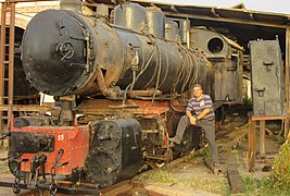 Locomotive à vapeur dans un atelier, à droite, un homme avec le pied droit posé sur la locomotive.