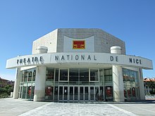 Vue d'une structure moderne ronde avec « Théâtre national de Nice » inscrit et dessus un toit plat octogonal.