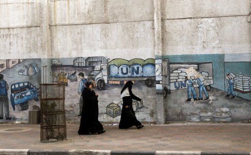 Palestinian women walk in front of graffiti next to the UN headquarters building in Gaza City on April 5, 2013. Gaza's Hamas rulers urged the United Nations to reconsider its suspension of food aid for Palestinian refugees, imposed after protesters stormed a UN depot. AFP PHOTO/MOHAMMED ABED